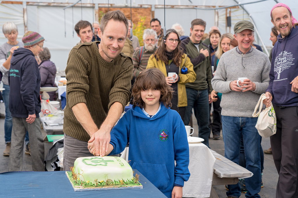 A Trees For Life volunteer and Invergarry Primary School pupil cutting the birthday cake