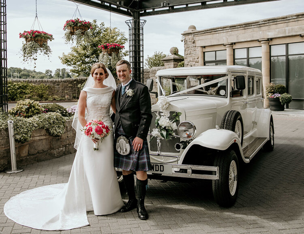 A happy bride and groom with their wedding car at the Old Course Hotel (Photo: Victoria Photograph)