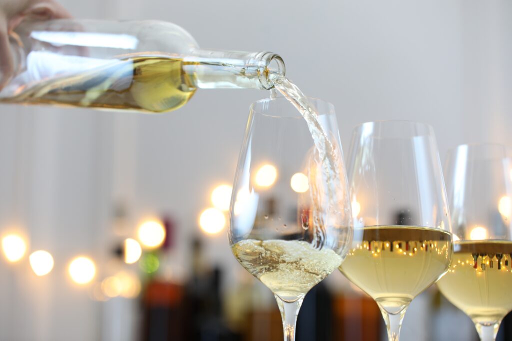 Pouring white wine into glass against blurred background with festive lights, closeup. Bokeh effect Credit: Adobe Stock