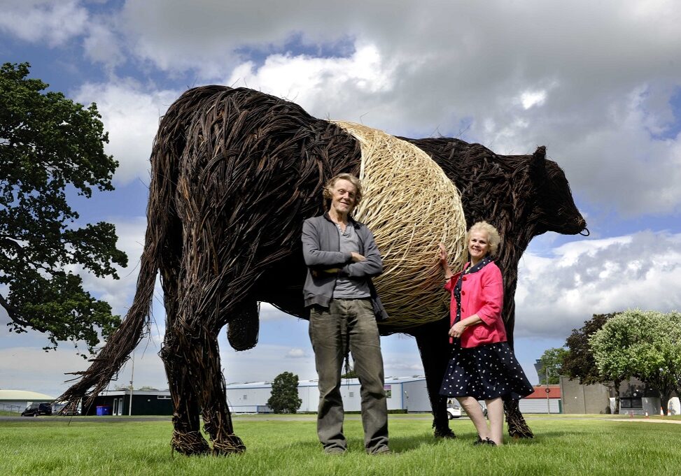 FREE PICTURE: Royal Highland Showcase Wicker Beltie and Tunnel Mural, Edinburgh, 14/06/2021:
Royal Highland Showcase Celebrates Dumfries and Galloway with One-Tonne Willow Bull:
A one-tonne wicker Beltie bull, hand sculpted in Dumfries and Galloway, has arrived in Edinburgh where it will be a centrepiece of this week’s Royal Highland Showcase - at the Royal Highland Showground on the fringes of Edinburgh 
Nearby, the famous underpass where the finest livestock are led in and out of the Ingliston showground arena, has been painted with a magnificent mural depicting farm animals, horses, wildlife and scenes from south-west Scotland.
 The Royal Highland Showcase runs online from today (Monday) 14th to (Sunday) 20th June (2021) and replaces the annual Royal Highland Show which cannot take place due to COVID-19 restrictions - see: https://www.royalhighlandshow.org 
 Each year RHASS invites a different region to act as “host”, allowing it to highlight the best of its rural economy. This year it’s the turn of Dumfries and Galloway which prides itself on its thriving creative community.
  Pictured with the beltie is artist Trevor Leat (correct), whose sculptures are familiar from Edinburgh’s Hogmanay celebrations, the Wickerman music festival and a variety of National Trust for Scotland properties. And artworks project leader Cathy Agnew (correct).
For more information see accompanying press release or contact  Matthew Shelley at Matthew@ScottishFestivalsPR.Org - 07786 704 299. 
 Photography for Royal Highland Society of Scotland (RHASS) from: Colin Hattersley Photography - www.colinhattersley.com - cphattersley@gmail.com - 07974 957 388.