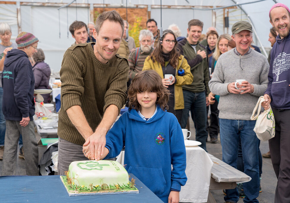 A Trees For Life volunteer and Invergarry Primary School pupil cutting the birthday cake